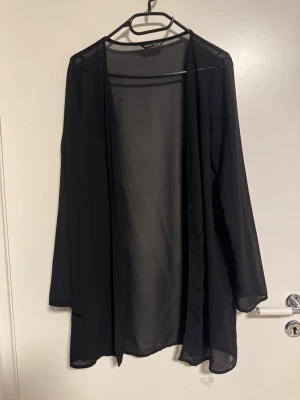 Svart transparent kofta från Shein - Säljer en svart, tunn och transparent kofta från Shein. Koftan har lång ärm och ett flowy, öppet fall utan knappar eller dragkedja. Perfekt att slänga över en topp för en chill och stilren look.