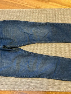 Blå jeans från Tommy Jeans, storlek 32 - Säljer ett par klassiska blå jeans från Tommy Jeans i storlek 32. Jeansen har raka ben, normal passform och snygga detaljer med logga på bakfickan. Tillverkade i slitstarkt denimtyg med kontrastsömmar och klassisk femficksdesign.