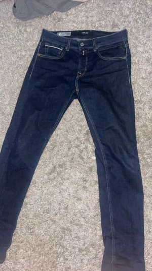 Replay Grover jeans i mörkblå denim - Säljer ett par Replay Grover jeans i mörkblå denim med snygga kontrastsömmar och klassiska bakfickor med broderad detalj. Modellen är rak och tillverkad i Replay Hyperflex-material som ger extra stretch och komfort. Perfekta för dig som gillar stilrena jeans med modern passform.