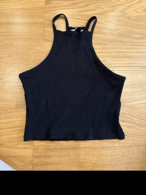 Svart ribbad croppad linnetopp Gina Tricot - Säljer en svart ribbad croppad linnetopp från Gina Tricot. Toppen har smala axelband och hög halsringning, vilket ger en sportig och clean look. Perfekt att matcha med jeans eller kjol för en enkel och snygg outfit.