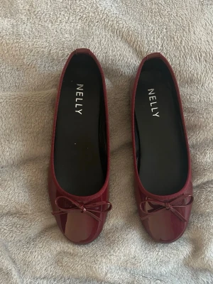 Vinröda ballerinaskor från Nelly - Säljer ett par vinröda ballerinaskor från Nelly med lackad finish och söt rosettdetalj. Dom är i storlek 40 men kan nog passa 39 också. Knappt använda! Helt slutsålda❤️