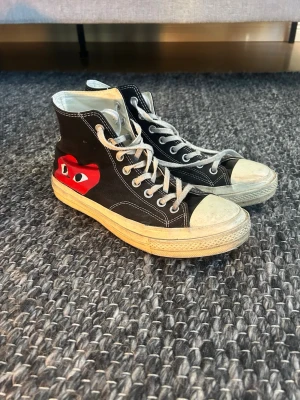 Cdg converse - Säljer ett par Converse Chuck Taylor All Star high tops i samarbete med Comme des Garçons Play. Skorna är svarta med vit sula, vita snören och den ikoniska röda hjärtloggan på sidan. Canvasmaterial och klassisk rund tå. Perfekta för dig som vill ha något unikt!