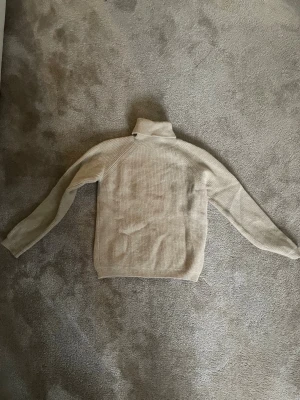 Beige polotröja i kashmir från Dal Lago - Supermjuk beige polotröja från Dal Lago, tillverkad i Italien. Tröjan är ribbstickad och har lång ärm samt hög polokrage. Perfekt för kalla dagar när du vill vara både stilren och bekväm.