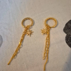 Guldpläterad örhängen med stjärnhänge - Snygga guldplatärad örhängen med små stjärnhängen och dubbla kedjor i olika länkar. Perfekt för dig som vill ha något trendigt och unikt med cool detalj. Passar till alla tillfällen när du vill sticka ut lite extra.