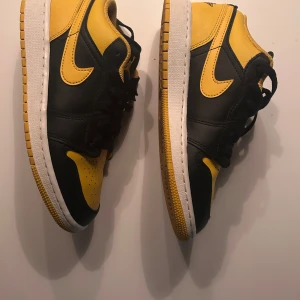 Nike Air Jordan 1 Low svart/gul - Storlek 36,5. Orginalbox medföljer. Nike Air Jordan 1 Low sneakers i svart och gul med klassisk Jordan-logga broderad på hälen. Skorna har snörning, perforerad tå och vit mellansula. Tillverkade i skinn med platt sula och rund tå. Snygg kontrast mellan färgerna och ikonisk design. Skorna är sparsamt använda, ett fåtal gånger. 