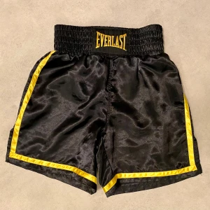 Everlast shorts - Säljer ett par boxningsshorts från Everlast. Shortsen är i storlek S och har en klassisk design med svarta shorts och guldfärgade detaljer. Perfekt för träning eller sparring. I mycket bra skick!