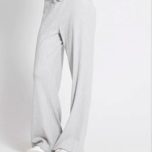 Ljusgrå ribbad långärmad tröja och byxor (set) - Superskön ljusgrå långärmad tröja med ribbad struktur och knappar vid halsen. Tröjan har en lätt croppad passform och vågig kant nertill för en chill vibe. Perfekt att matcha med tillkommande byxor.