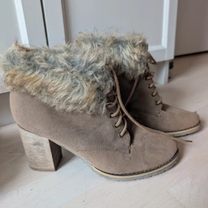 Bruna boots med fuskpäls från Din Sko - Säljer ett par bruna boots från Din Sko i storlek 39. Skorna har snörning, grov klack och är fodrade med mjuk fuskpäls upptill. Utsidan är i mockaimitation och klacken är robust och träfärgad. Perfekta för kyliga dagar när du vill vara både varm och snygg.