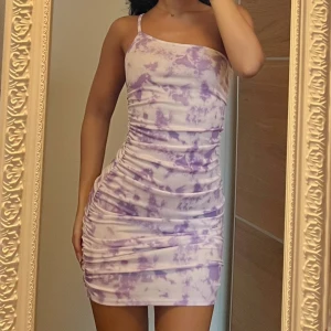 Lila och vit tight kortklänning -  kort klänning med lila och vitt batikmönster. Tight passform, ärmlös med smala axelband och rynkade sidor 