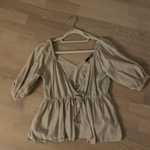 Beige omlottblus från Bik Bok XS - Säljer en beige omlottblus från Bik Bok i storlek XS. Blusen har trekvartsärmar med resår, v-ringad omlottfront och knyt i midjan. Tillverkad i ett lätt linnematerial som ger en chill och flowy vibe. Perfekt att styla med jeans eller kjol för en snygg look.