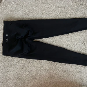 Relode Aura tights - Snygga svarta leggings från Relode med hög midja och tight passform. De är tillverkade i ett stretchigt syntetmaterial som sitter skönt och följer kroppens former. Perfekta för träning eller chill dagar. Relode-logga på linningen ger en sportig vibe. Storlek s / regular