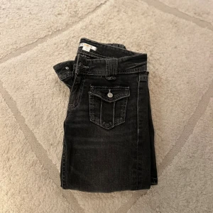 Gina Tricot Svarta jeans med slitningar och raka ben - Säljer ett par svarta jeans med coola slitningar på framsidan och raka ben. Jeansen har framfickor med lock och knapp, klassisk femficksdesign och kontrastsömmar. Perfekt för dig som gillar en edgy stil och vill ha något som sticker ut.