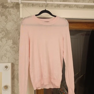 Ljusrosa stickad tröja från 157 XS - Supersöt ljusrosa stickad tröja från 157 i storlek XS. Tröjan har rund hals, långa ärmar och ribbade muddar vid ärmslut och nederkant. Perfekt för dig som gillar mjuka och stilrena plagg i en feminin ton😊