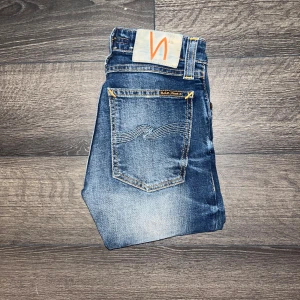 Nudie Jeans Skinny Lin  - Snygga Skinny Lin jeans från Nudie Jeans i mörkblå tvätt med slitningar och klassiska orange sömmar. Modellen är skinny. Midja 30cm, längd 93cm. JAG SKICKAR EJ FLER BILDER NÄR JAG BÄR JEANSEN! för storleksguide hänvisar jag till måtten och för bättre inblick i passformen rekommenderar jag att googla på modellnamnet. Jeansen kan vara uppsydda utan att jag noterat det så kolla måtten noggrant :) s3