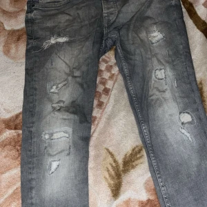 Grå skinny jeans med slitningar W32/L32 - Snygga grå skinny jeans från Denim Co i storlek W32/L32. Jeansen har flera slitningar och lagade hål på framsidan för en cool, edgy look. Klassisk femficksmodell med normal passform och smal siluett. Perfekt för dig som gillar streetstyle.