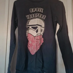 Svart långärmad tröja Spoil Troopers - Svart långärmad tröja med tryck av en stormtrooper med röd bandana och texten 'Spoil Troopers' på bröstet. Perfekt för dig som gillar unika prints och Star Wars-inspirerade plagg. Trycket är lite blekt i färgen men inga andra skavanker vad jag har kunnat se.