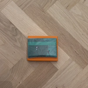 Grön plånbok med golfmotiv - Snygg grön plånbok med golfinspirerat motiv. Plånboken har flera fack för kort och är tillverkad i exklusivt skinn med detaljer i olika färger. Perfekt för dig som vill ha något unikt och sportigt i fickan.