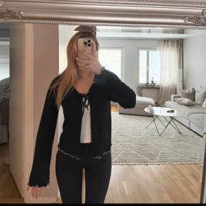 Svart ribbad knytblus/kofta - Svart långärmad ribbad kofta med v-ringning och knyt framtill. Toppen har vågig kant med vit kontrastsöm längs nederkanten och ärmarna. Endast använd 1 gång 🌸