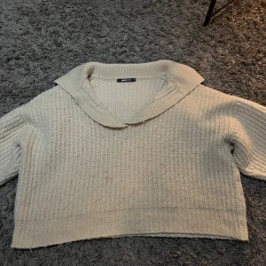 Beige stickad tröja från Gina Tricot - Säljer en beige stickad tröja från Gina Tricot i storlek M. Tröjan har en bred krage och ribbade detaljer vid ärmslut och nederkant. Modellen är croppad och har långärmade armar, perfekt för att ge en chill och snygg look.