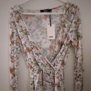 HELT NY OANVÄND vit och blommig omlott topp från Bik Bok, Small - Helt ny oanvänd supersöt omlott-topp från Bik Bok med blommigt mönster i pastelliga toner av tex rosa,  lila och, grön. Toppen har v-ringning, långa ärmar och markerad midja. Perfekt för vår och sommar, i mjukt och lätt material. Storlek Small. Felfri.