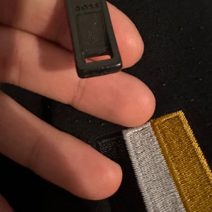 Svarta mjukisbyxor från BOSS - Svarta mjukisbyxor från BOSS med broderad logga och färgblock i vitt, gult och svart på benet. Byxorna har elastisk midja och dragkedjor vid fickorna. Perfekta för chill eller träning, riktigt snygga detaljer och skön passform.