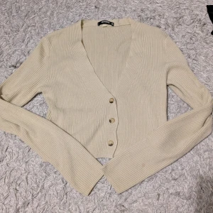 Ribbad beige kofta - Superfin ribbad kofta i beige. Croppad modell med v-ringning och tre snygga knappar framtill. Långärmad och i mjukt stickat material, perfekt för lager-på-lager under hösten eller våren. En liten fläck på ena armen bara☺️