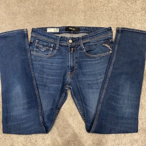 Replay Anbass Jeans - Snygga mörkblå jeans från Replay med klassisk femficksdesign och slim fit. Jeansen har diskreta slitningar och kontrastsömmar, samt Replay-logga på fickan. Perfekta för dig som gillar en stilren och tidlös look.