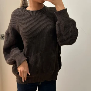 Mörkbrun stickad oversized tröja - Säljer en mörkbrun stickad tröja med grov ribbad struktur och rund hals. Tröjan har långa, breda ärmar och en loose, oversized passform som ger en chill vibe. Perfekt att matcha med jeans eller leggings för en avslappnad look.