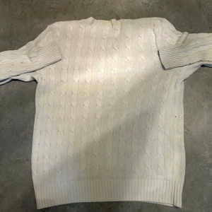 Vit kabelstickad tröja Polo Ralph Lauren XS - Kabelstickad vit tröja från Polo Ralph Lauren i storlek XS. Klassisk rund halsringning, ribbade muddar och nederkant samt broderad marinblå logga på bröstet. Perfekt för lager-på-lager och snygg till jeans eller mjukis