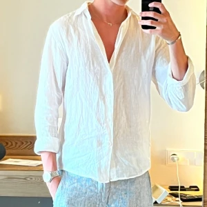 Vit linneskjorta från Uniqlo - Säljer en stilren vit skjorta från Uniqlo i luftig linne. Skjortan har klassisk krage, knäppning framtill och långa ärmar. Perfekt för en clean och avslappnad look under varmare dagar.