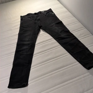 Svarta Replay jeans straight fit - Svarta jeans från Replay med klassisk femficksdesign och raka ben. Byxorna har en stilren look med svarta sömmar och Replay-logga på bakfickan. Perfekta för dig som gillar en enkel och tidlös stil.