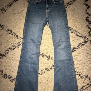 Bootcut jeans blå denim - Säljer ett par jeans med bootcut passform. Jeansen har fem fickor, normal midja och är tillverkade i slitstark denim. Snyggt utseende med lätt tvättad look. Perfekt för dig som gillar retrostil och vill ha ett par jeans med lite extra vidd vid benslutet.
