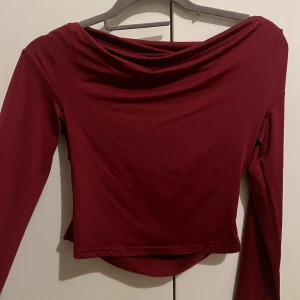 Vinröd långärmad polotopp - Säljer en vinröd långärmad polotopp med snygg draperad halsringning. Toppen har en tight passform och är tillverkad i ett mjukt, stretchigt material som känns skönt mot huden. Perfekt för dig som gillar stilrena och trendiga plagg med en twist. Helt ny. 