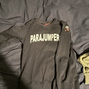 Svart sweatshirt från Parajumpers - Svart sweatshirt från Parajumpers med stor vit logga på bröstet och patch på ena ärmen. Klassisk rund hals och långa ärmar. Mjuk och skön bomullskvalitet, perfekt för chill dagar. Snygg och enkel design som funkar till jeans eller joggers. nypris 1800