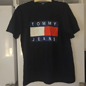 Svart t-shirt med logga - Svart t-shirt med stor klassisk logga framtill i vitt, rött och blått. T-shirten har rund hals och korta ärmar. Perfekt för dig som gillar streetwear och vill ha en ikonisk look. Passar även M