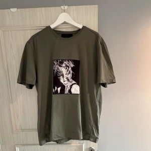 Olivgrön t-shirt Limitato x Ellen von Unwerth - Olivgrön t-shirt med rund hals och korta ärmar från Limitato x Ellen von Unwerth. Framsidan har ett svartvitt fotoprint med konstnärligt motiv. T-shirten är gjord i mjuk bomull. Dessvärre med liten missfärgning vid halsen, annars knappt använd. Pris kan diskuteras, hör av dig vid minsta fråga!