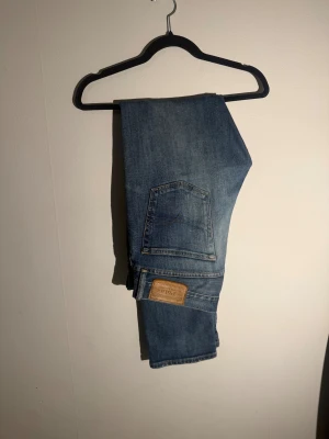 Blå jeans från Polo Ralph Lauren - Snygga blå jeans från Polo Ralph Lauren med klassisk femficksdesign och raka ben. Jeansen har en mellanblå tvätt med lätt slitning och detaljerade sömmar. Märkespatch i läder baktill i midjan och dragkedja i gylfen. Perfekta för en avslappnad stil.