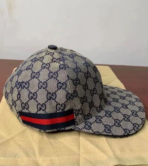 Gucci keps - Säljer en snygg Gucci keps i beige med klassiskt GG-monogram i mörkblått. Kepsen har en röd och marinblå rand på sidan. Perfekt accessoar för att lyfta din outfit med lyxig streetstyle. 