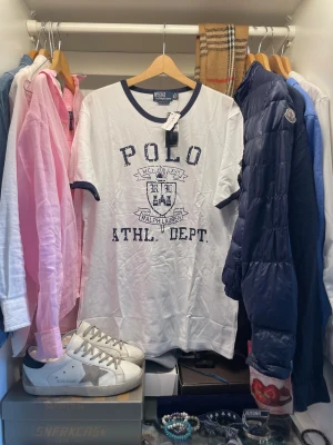 Vit t-shirt Polo Ralph Lauren XXL - Vit t-shirt från Polo Ralph Lauren med mörkblå detaljer vid krage och ärmslut. Stor tryckt logga och emblem framtill. Tillverkad i mjuk bomull. Perfekt t-shirt till vardagen. Nypris runt 1300kr. Aldrig använd och har pristagarna kvar.                      Skriv vid frågor, priset är inte hugget i sten 🤝