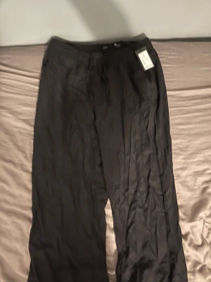 Svarta linnebyxor från lager  157, stl S - Svarta linnebyxor från 157 med avslappnad passform och resår i midjan. Byxorna har snörning i midjan för extra komfort och är tillverkade i ett lätt och luftigt linnematerial. Perfekta för en chill och stilren look. Aldrig använt med prislapp, skulle säga att byxorna är större en vanlig S, kostade (200kr) från början 