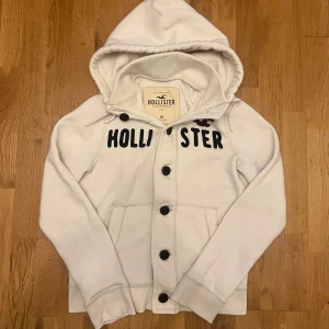 Vintage Hollister cardigan / kofta med knappar - Vit hoodie från Hollister i storlek M med svart text på bröstet och Hollister-logga i vinrött. Tröjan har huva med snörning⚪️|                                           Just dessa tröjor är väldigt eftertraktade!!                          Skriv vid minsta fundering                                 Priset kan självklart diskuteras 
