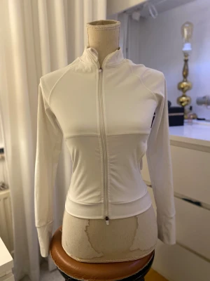 Vit träningsjacka långärmad - Tajt vit träningsjacka i gott skick från ”Pretty little thing” i storlek 36, men är liten i storlek! Bra skick annars och knappt använd.