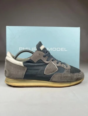 Grå-blå sneakers från Philippe Model - Snygga sneakers från Philippe Model i en mix av grått och blått med beige detaljer. Ovandelen är tillverkad i mocka och textil, med klassisk snörning och platt sula. OBS: Box medföljer ej vid köp!