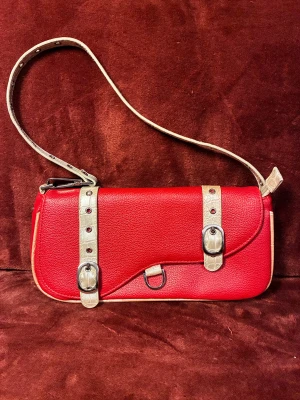 Elvis Presley väska i 90-talsstil - Vintage Elvis Presley-väska, i mycket gott skick, inga tecken på slitage, som ny. Röd färg, med krämfärgade detaljer. Du hittar inget liknande någon annanstans😉