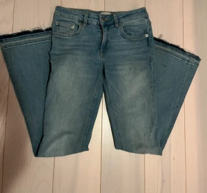 Blå bootcut jeans med rå kant - Snygga blå bootcut jeans från H&M med klassisk femficksdesign och rå, fransad kant vid benslut. Jeansen har en liten sliten detalj på ena benet och är tillverkade i mjukt denim med lätt tvättad look. Perfekt för dig som gillar avslappnad stil.