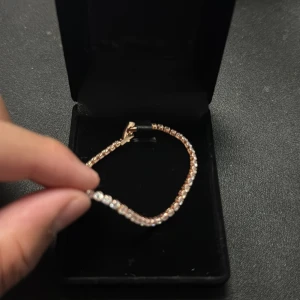 Rose Guldigt  tennisarmband med stenar - Ett elegant tennisarmband i rosa guld platering med gnistrande vita stenar längs hela bandet. Armbandet har en klassisk och tunn design som ger en lyxig känsla. Perfekt för dig som gillar stilrena smycken med extra bling. L 17cm, Bredd 2,5mm, stenar zirconia kommer utan box