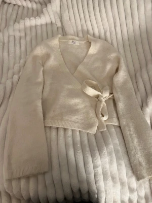 Vit omlottkofta från Gina Tricot XS - Superfin vit omlottkofta från Gina Tricot i ullblandning. Koftan har lång ärm, croppad passform och knyt i sidan. Perfekt för lager-på-lager och ger en mysig vibe till din outfit. En liten fläck vid armbågen (sista bilden)