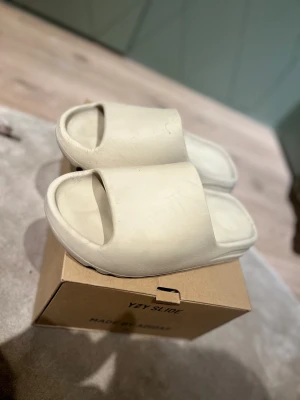 Adidas Yeezy Slide beige  - Säljer ett par Adidas Yeezy Slide i beige färg. De har en chunky, modern design med öppen tå och platt sula. Tillverkade i syntetmaterial med en mjuk och bekväm känsla. Perfekta för chill dagar och har den klassiska Yeezy-viben. Storlek 43 äkthet bevis finns 