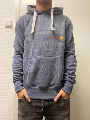 Hoodie från Superdry  - Fet hoodie från Superdry. Lite slitet tryck annars bra skick. Modellen är 173cm, 64kg. Pris kan diskuteras!