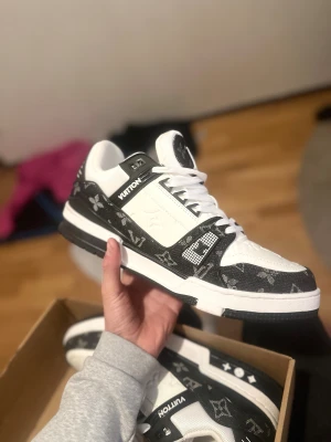 Valentino Garavani Open sneakers vit/blå - Snygga Valentino Garavani Open sneakers i vitt skinn med bred mörkblå rem över snörningen. Klassisk rund tå, platt sula med pyramidmönster och vita skosnören. Guldlogga på plösen och coola detaljer på hälen. Perfekt för dig som gillar exklusiv streetstyle.